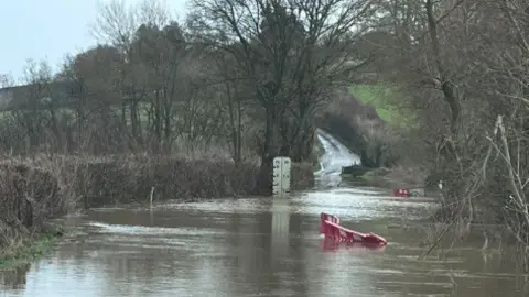 A flooded country road with construction barriers submerged in the water