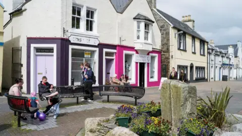 Getty Images A generic photo of Stornoway on the Isle of Lewis, you can see some people sitting on a black bench and some brightly coloured shop fronts in the foreground