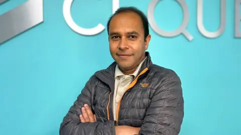Seguridad de Cequence con una chaqueta Puffa y con su archivo de brazo de Shreyans Mehta se encuentra frente a un fondo azul.