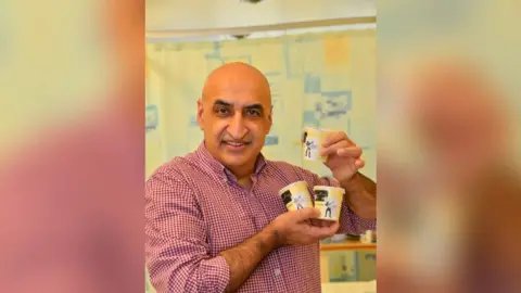Nottingham University Hospitals NHS Trust Professor Opinder Sahota stood holding some tubs of "N-ICE Cream", smiling at the camera.