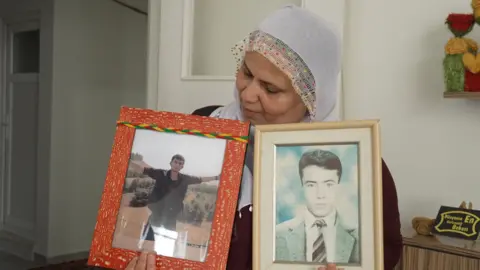 BBC/Ozgur Arslan Menice stands with framed pictures of two young people. Look at the bottom of the image on its right.