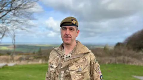  Col Jim Bird looking and smiling at the camera. He is wearing a beret and uniform. 
