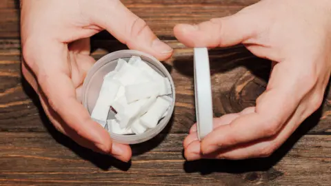 Getty Images A young person opens a tin of nicotine pouches - small, white sachets containing nicotine - the hands are visible only