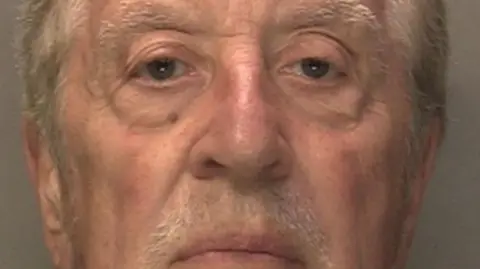 West Midlands Police An old man with white short hair and a moustache is looking at the camera. He isn't smiling. It is a mug-shot, so the background is plain. 