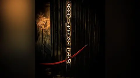 Continental Club, Dabbz Photography The entrance to the Continental Club in Manchester. There is a red rope across the doorway and a vertical backlit sign spelling out the venue's name on on the wall to the right.