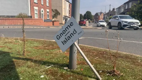 The Gnome Island sign, leaning up against a metal pole