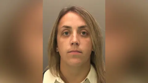 Police custody image of Danielle Barrett. She has long fair hair and is wearing a yellow shirt, which is open at the collar. She is looking directly at the camera.