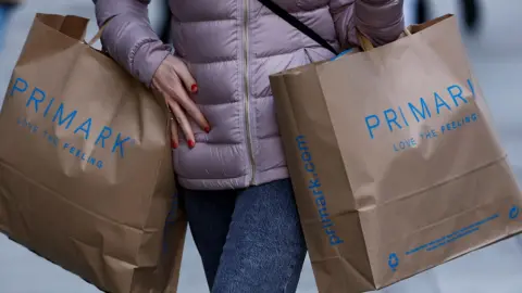 BBC A close up shop of a woman in a purple puffa coat carrying two Primark shopping bags