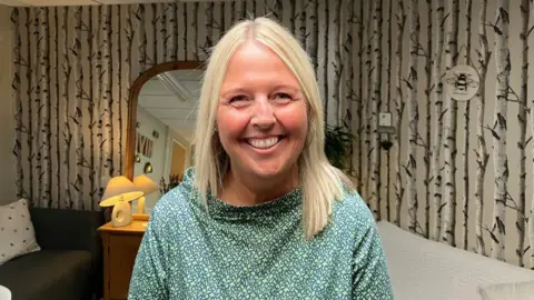 Ash McGann, headteacher at Burton Green Primary School. She has shoulder-length blonde hair, and wears silver hoop earrings and a green patterned dress.