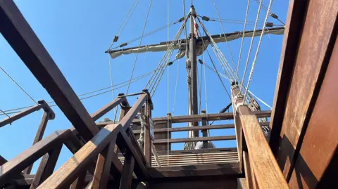 George Carden/BBC A view from one of the lower decks looking up the stairs at the front mast which has the sail up and ropes coming across