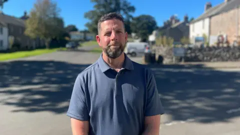 Man centred in image with blurred background of main road running through village