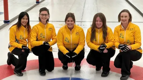 Helen Williams A line-up of women in yellow Australia tops on a curling rink