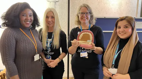 Four dental health specialists from Swindon Borough Council and Great Western Hospital NHS Foundation Trust smile and hold a large model mouth with a toothbrush