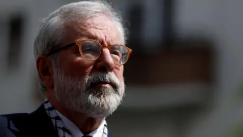 Gerry Adams in a blue suit with white shirt and scarf.