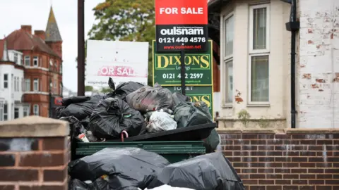 EPA/Shutterstock Uncollected rubbish is seen in the Balsall Heath area of Birmingham on 10 September 2025. Black bags are piled up over a wall near houses, which have For Sale signs in front of them.