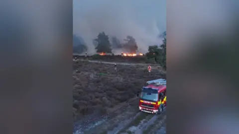 Fire engine at heathland wildfire with firefighters battling flames