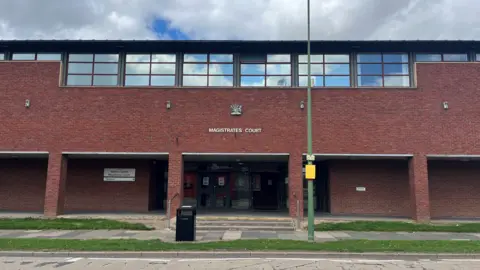 BBC Newton Aycliffe Magistrates' Court. The building is made of red brick and has a sign showing its name and a black bin out front.