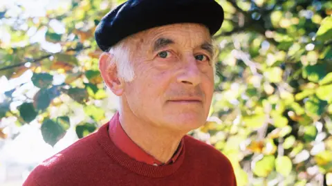 Supplied Michael Laskey, wearing a beret, looks at the camera. There is a tree in the background.