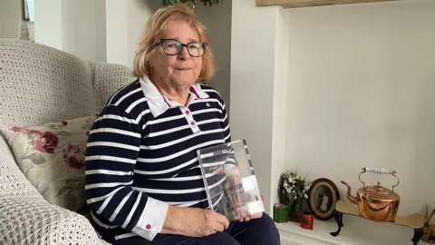 A woman holds a curved glass trophy and smiles for the camera