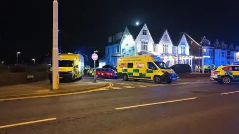 The Blackpool Lads A number of yellow and green ambulances and advanced paramedic vehicles are parked on a wide road. 
