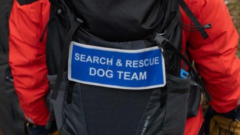 Back of a person with with serch and rescue dog team written on he back of a bag