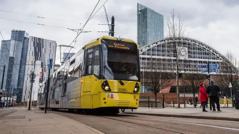 Getty Images A yellow Manchester tram driving past with some modern skyscrapers in the background