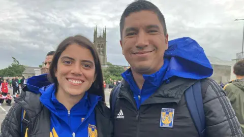 A woman and a man pose for a photo. They're smiling. They're wearing sport gear. A church is in the distance.