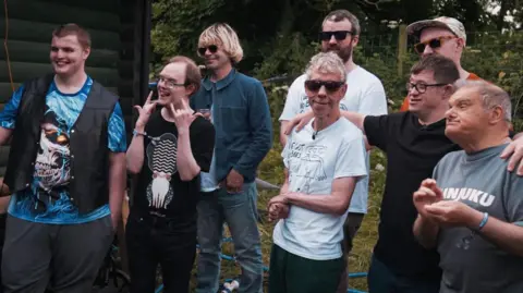 A mixed age group of men, some with disabilities, stand alongside each other smiling.