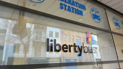 BBC Glass private tinted wall with black libertybus sign in the middle, dark blue sign above saying LIBERATION STATION and a bus emoji in a circle in dark blue