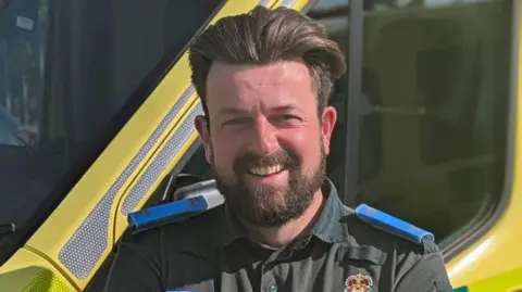 Luke Rapela - a young man with brown hair combed back and a short beard 