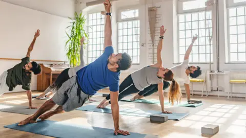 Stock image of six people doing pilates in a brightly lit studio