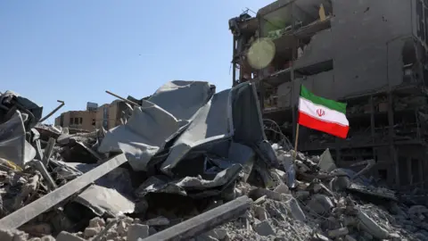 Reuters The national flag of Iran flies in the wind as debris lies scattered in the aftermath of an Israeli and U.S. strike on a police station, amid the U.S.-Israeli conflict with Iran, in Tehran, Iran, March 3, 2026.