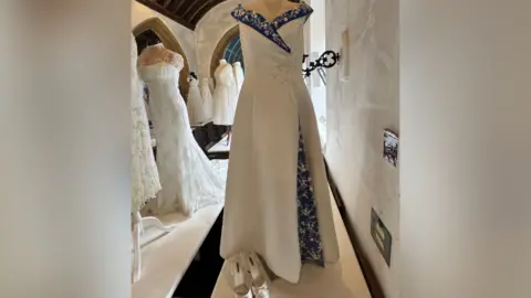 St Catherine's Church A white wedding dress with blue details is displayed on a mannequin in a church.