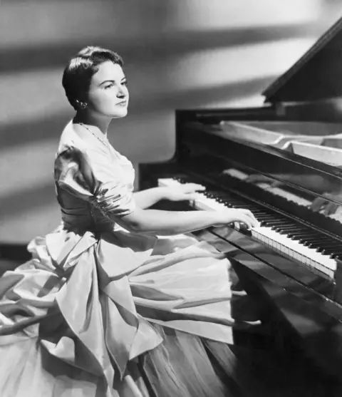 Getty Images Ruth Slenczynska sits at the piano during a concert in 1958, as she made her second debut. She is wearing a voluminous ballgown, with her fingers resting on the keys