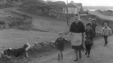 Woman walking along country road with children and a dog