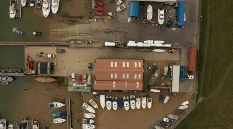 Ben Bradley A drone shot of the boatyard shows a number of small vessels on dry land, several cars and workshop buildings.
