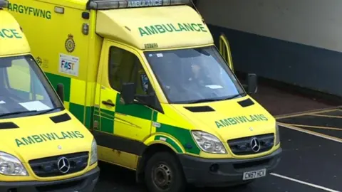 BBC A close up of two yellow and green ambulances parked next to each other in a car park