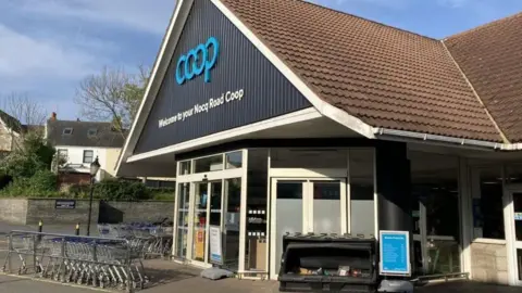 BBC A Coop store from the outside with trolleys parked at the entrance. 
