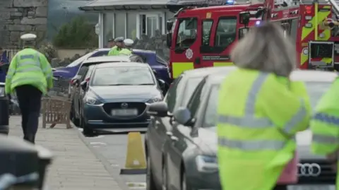 Police working at the scene in Beaumaris. Cars are parked on the street and a fire engine is in the background 