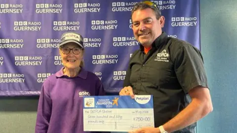Yvonne Chauvel, who wears a purple GSPCA jumper and shirt as well as a GSPCA cap, stands next to GSPCA manager Steve Byrne, who holds a big cheque for £750.