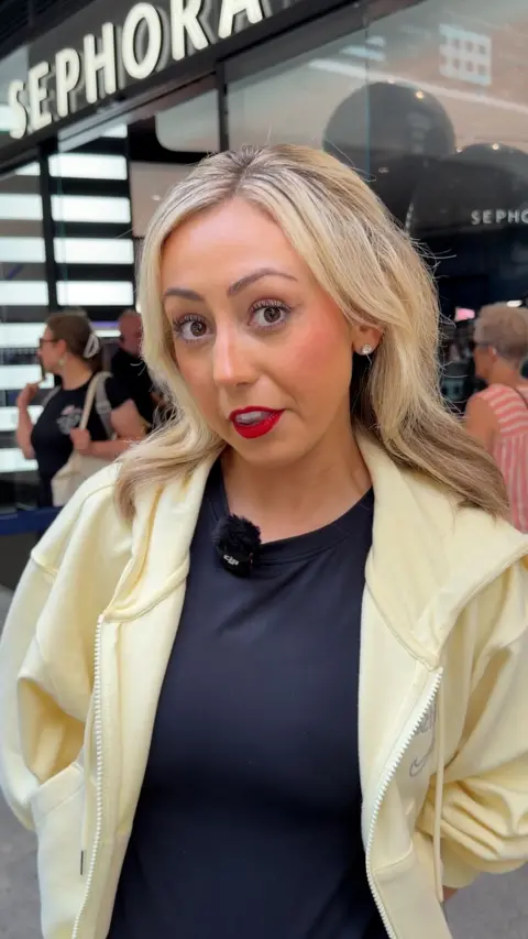 Young woman with blonde hair and red lipstick standing outside a Sephora make up shop