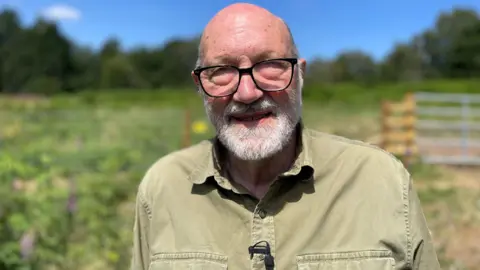 Older man with beard, glasses and khaki shirt in open countryside