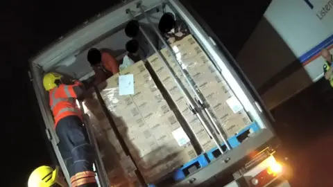 Cambs Police A firefighter is on a ladder helping men who are sat on pallets of Nutella chocolate spread in the back of a lorry. The faces of the men have been blurred