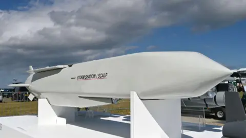 Getty Images A Storm Shadow cruise missile, which is several metres long and has a white glossy outer layer, as well as a "Storm Shadow/SCALP" logo, pictured on a display stand at an air show in Farnborough 