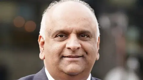 PA Media An image of County Councillor Azhar Ali. He is smiling, and wearing a blue suit with a white shirt.