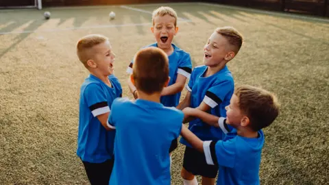Getty Images Group of junior soccer team players huddling on sports field - stock photo