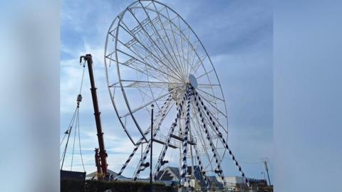 Large big wheel with sea in background and crane in foreground
