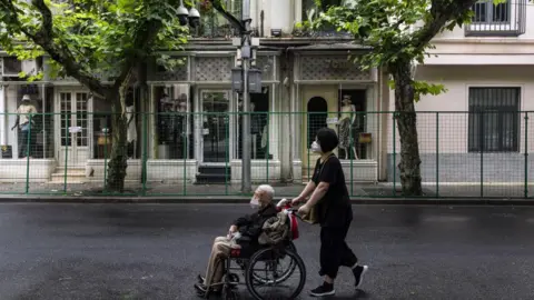 Getty Images A woman wheels a man in a wheelchair past a fence surrounding a neighborhood placed under lockdown due to Covid-19 in Shanghai, China, on Friday, June 10, 2022. 