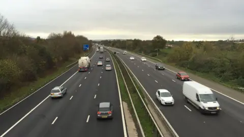 A photo showing both sides of a motorway, with traffic travelling along three lanes on both sides.