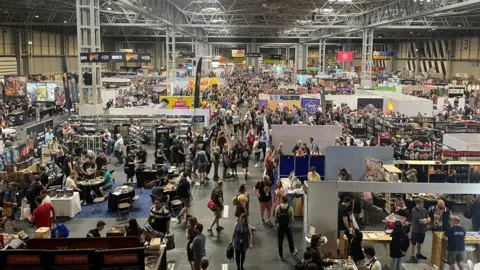 A crowded exhibition hall with people milling around and looking at various displays.